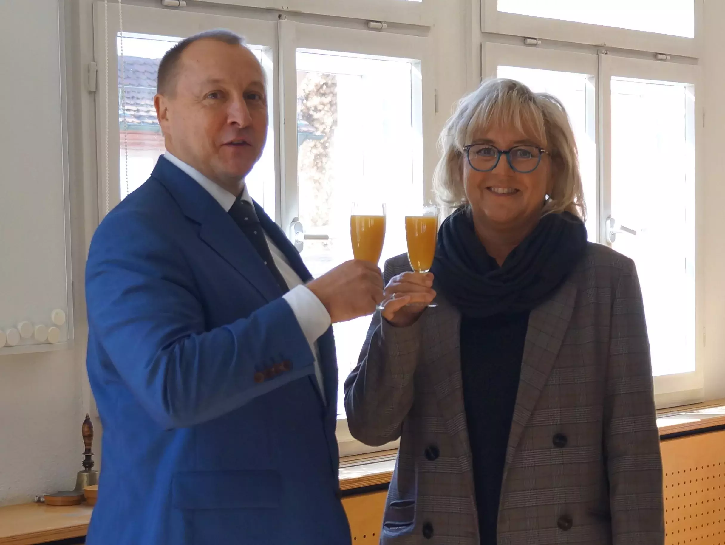 Jörg Kotzur und Christine Seehann stoßen mit einem Glas Orangensaft an und lächeln in die Kamera.